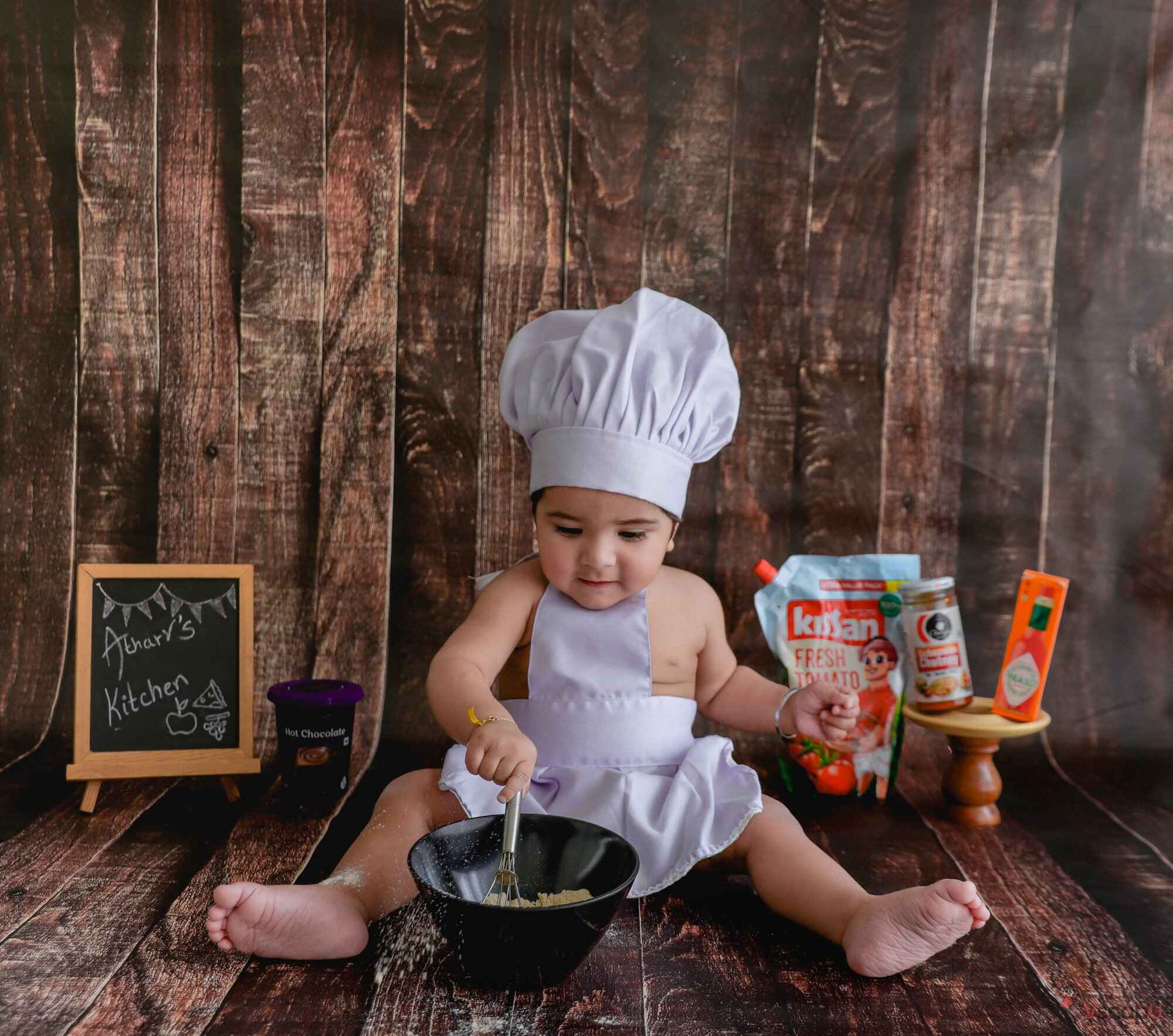 Adorable baby girl as a little chef, playing with a board in a heartwarming baby photoshoot.